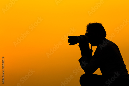 Silhouette of a man photographer with DSLR camera and tele lens at sunset on rooftop. Photographer life concept.