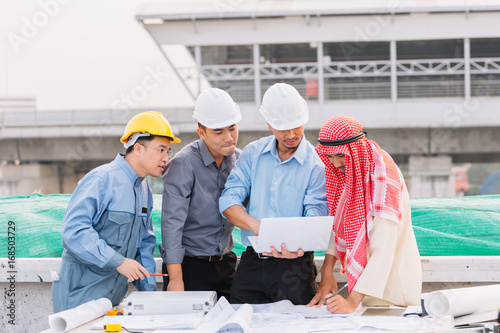 Arabian businessman and Engineer and Laborer working and discussion with laptop  on construction plans front of building in his work site. Teamwork concept