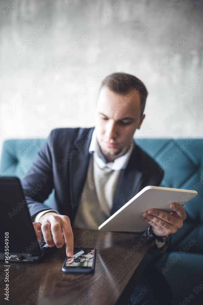 Young, modern and serious business man sitting in cafe and doing his job on notebook, cellphone and tablet. Young, modern and serious business man sitting in cafe and doing his job on notebook, cellphone and tablet.