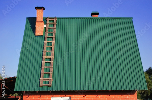 Green metal roof on the house, with a brick pipe and a wooden staircase
