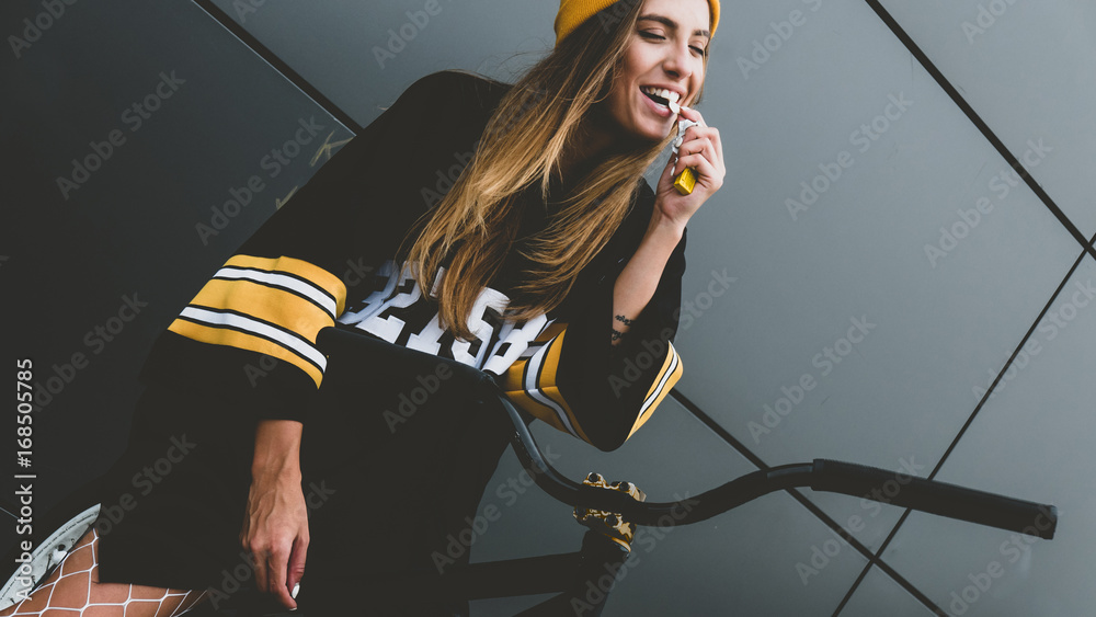 Outdoor lifestyle portrait of pretty sexy lookin young girl in hockey  jersey style dress posing on gray wall background with street bicycle Stock  Photo