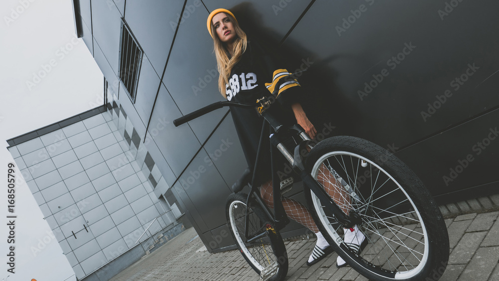 Outdoor lifestyle portrait of pretty sexy lookin young girl in hockey jersey  style dress posing on gray wall background with street bicycle Stock Photo