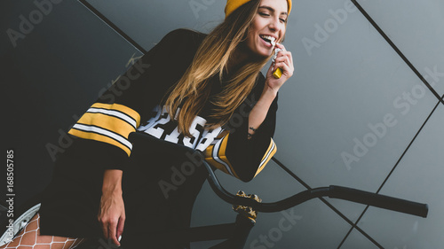 Outdoor lifestyle portrait of pretty sexy lookin young girl in hockey jersey style dress posing on gray wall background with street bicycle photo