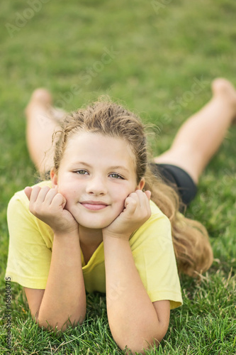 A young, pretty girl dressed in sportswear lying on green lawn at summer day