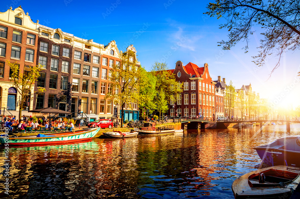 Traditional old buildings and and boats in Amsterdam, Netherlands at sunset. Canals of Amsterdam.