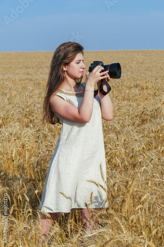 Pretty girl taking photos with big black camera on the field © PaulShlykov