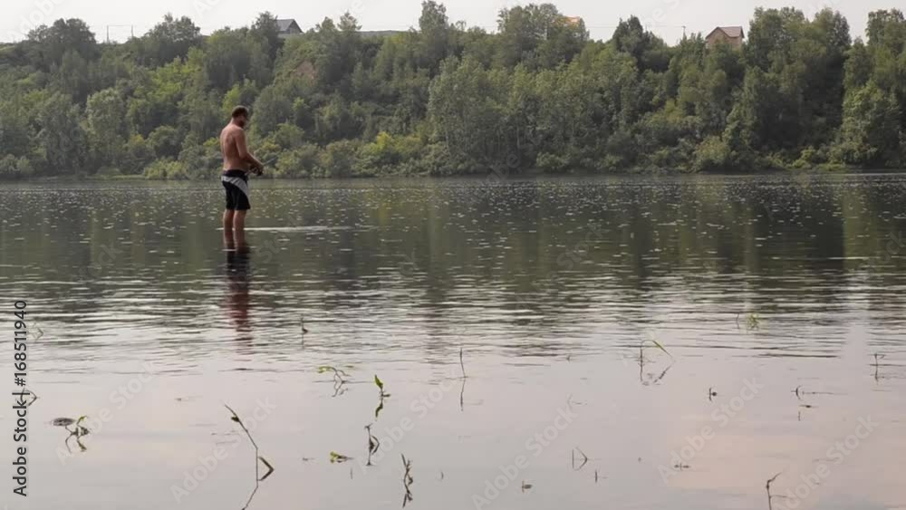 half-naked fisherman with a fishing rod fishing in the calm river half-naked fisherman with a fishing rod fishing in the calm river