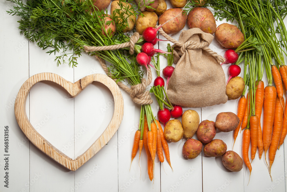 Rustic style. Fresh potatoes, carrots, radish and heart white wooden background