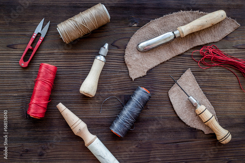 Leather craft accessories. Tools and matherials on dark wooden background top view photo