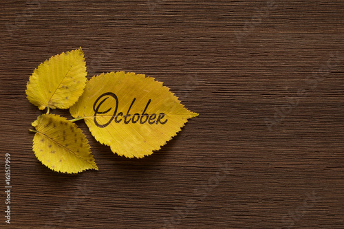 Golden leaves with the inscription OCTOBER on the brown wooden background.