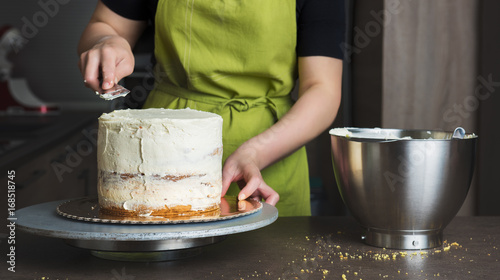 Billede på lærred Unrecognisable woman decorating a delicious layered sponge cake with icing cream