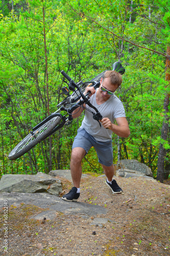A bicyclist in glasses rises with a mountain bike across the rough terrain. Taking sports in nature. Healthy way of life 