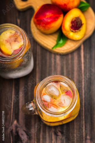 Mason jar glass of homemade peach iced water on a rustic wooden background. Top view.