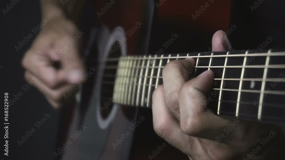 Man playing acoustic guitar on black background with fingers in slow motion
