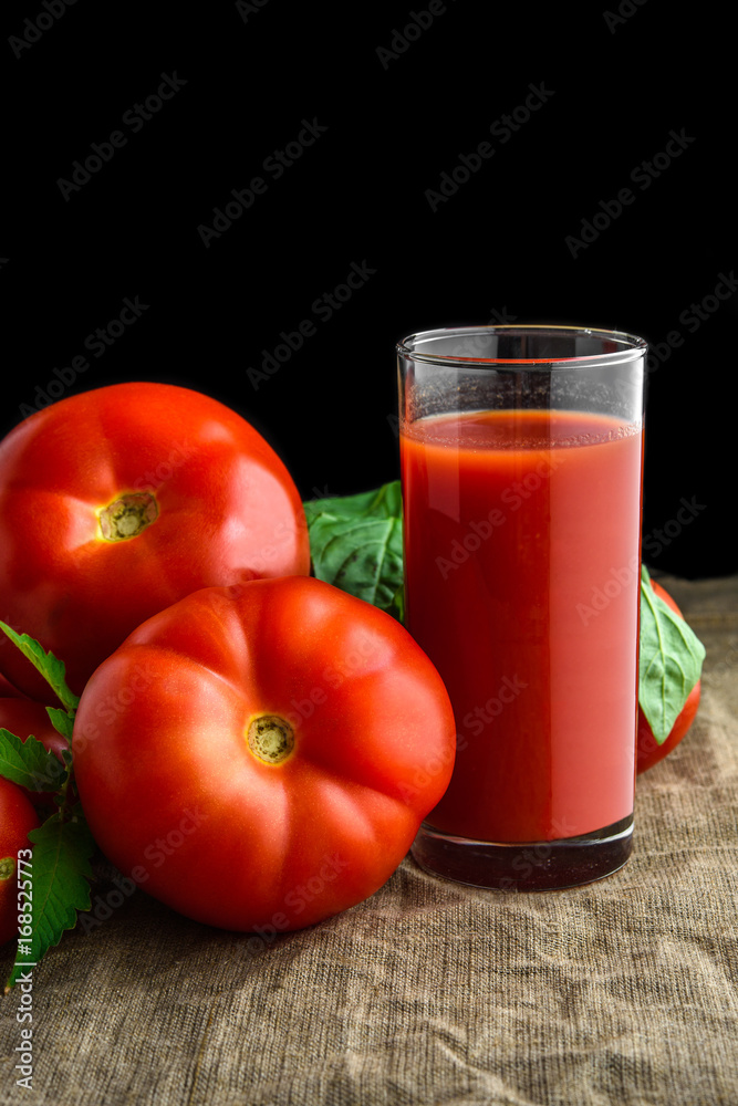 Organic tomato juice in glass and fresh tomatoes with green leaves on dark Organic tomato juice in glass and fresh tomatoes with green leaves on dark