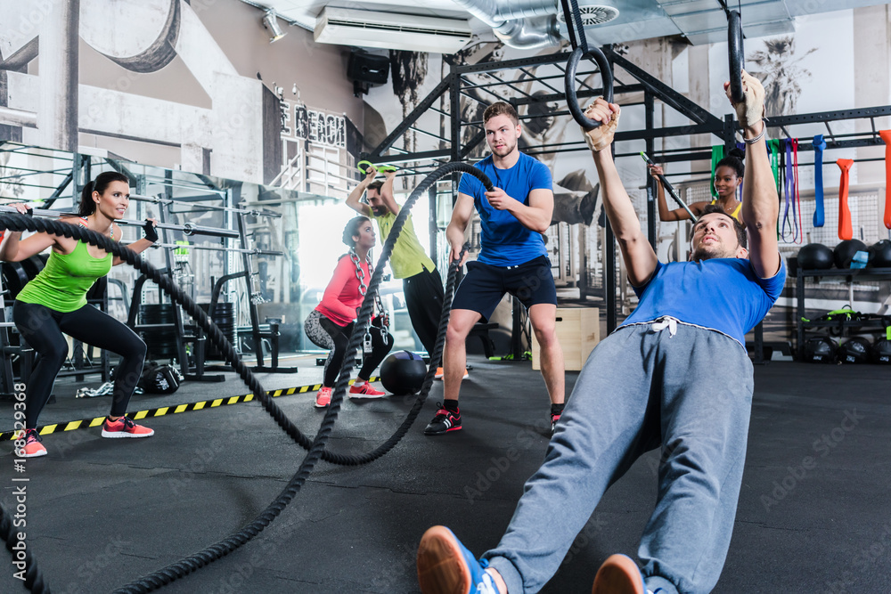 Fototapeta Mężczyźni i kobiety wykonujący treningi crossfit na siłowni uprawiają sport w zapaśnictwie i na linach