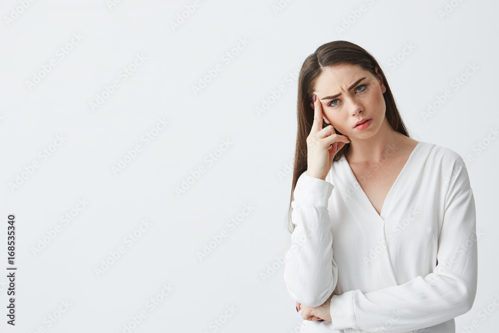 Displeased young beautiful businesswoman thinking looking at camera with finger near temple over white background. Displeased young beautiful businesswoman thinking looking at camera with finger near temple over white background.