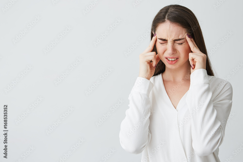 Young beautiful brunette businesswoman holding fingers on temples frowning from pain over white background. Headache. Young beautiful brunette businesswoman holding fingers on temples frowning from pain over white background. Headache.