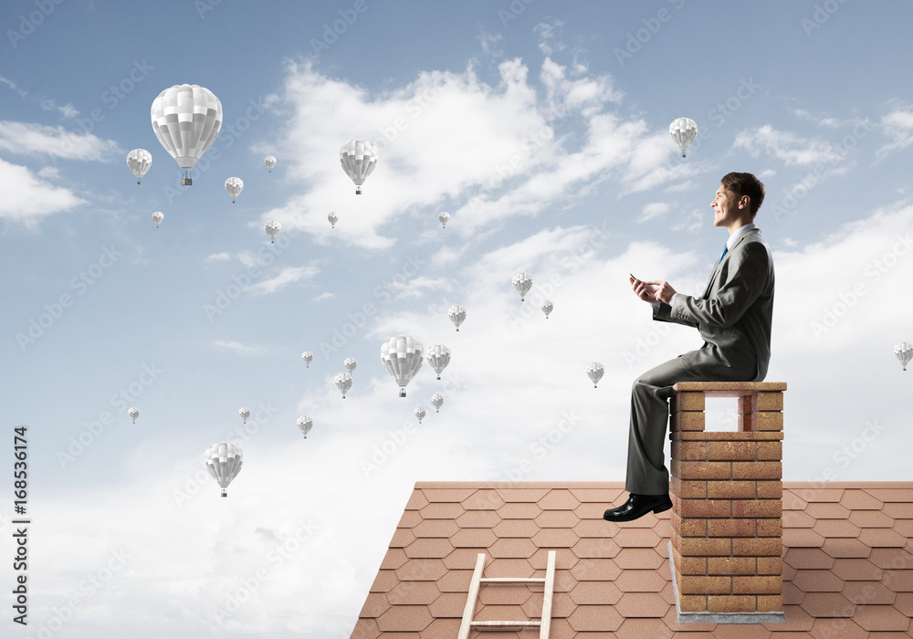 Man on brick roof using smartphone and aerostats flying in air