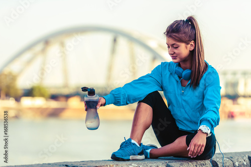 Young woman jogger resting drinking water by the river