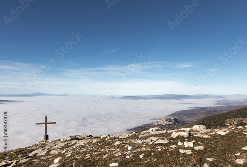 A wooden cross on top of Subasio mountain, with a sea of fog below and Assisi town (Umbria) in the background