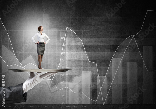 Confident elegant businesswoman presented on metal tray and graphs at background