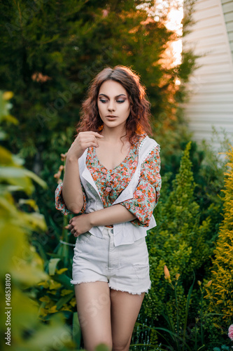 Beautiful young woman in romantic styled white shorts, blouse and vest on foliage background. Perfectly retouched.
