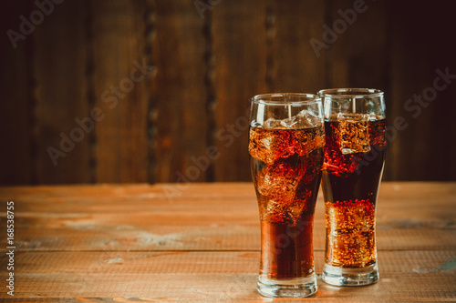 Beautiful cold fizzy cola soda with cubes ice in glasses goblet on old wooden background with free space