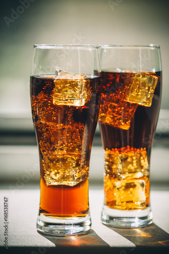 Beautiful cold drink of Cola with ice cubes in a glass on a grey window background with free space