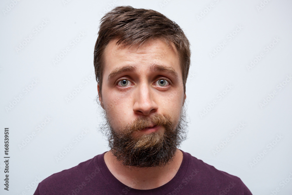 Young bearded man uncertain what to do with his messy beard and moustache - obrazy, fototapety, plakaty 