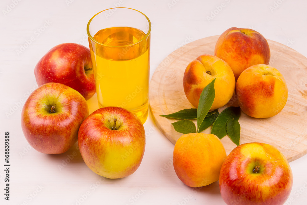 Glass of juice and ripe apples and peaches on a wooden table. Juice and fresh fruits on a light background. Glass of juice and ripe apples and peaches on a wooden table. Juice and fresh fruits on a light background.