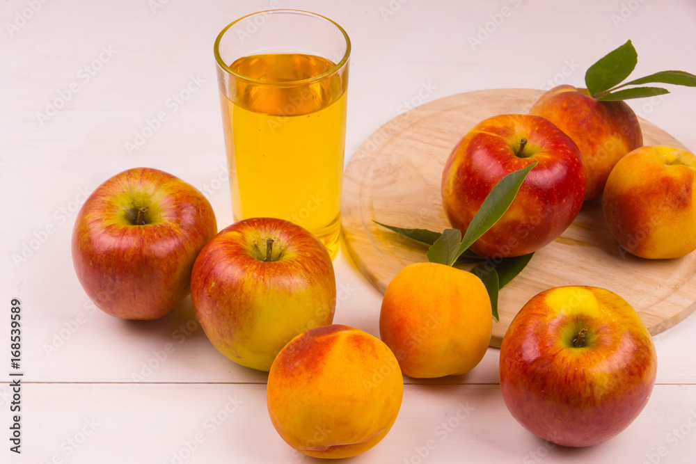 Glass of juice and ripe apples and peaches on a wooden table. Juice and fresh fruits on a light background. Glass of juice and ripe apples and peaches on a wooden table. Juice and fresh fruits on a light background.