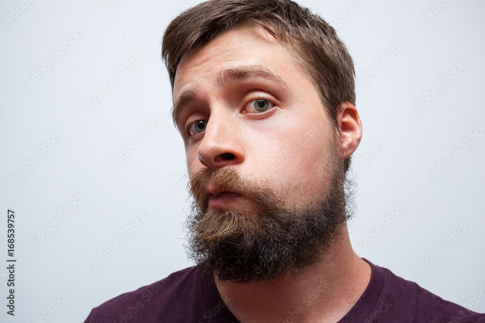 Young bearded man looking at his messy long beard and moustache in the mirror - obrazy, fototapety, plakaty 