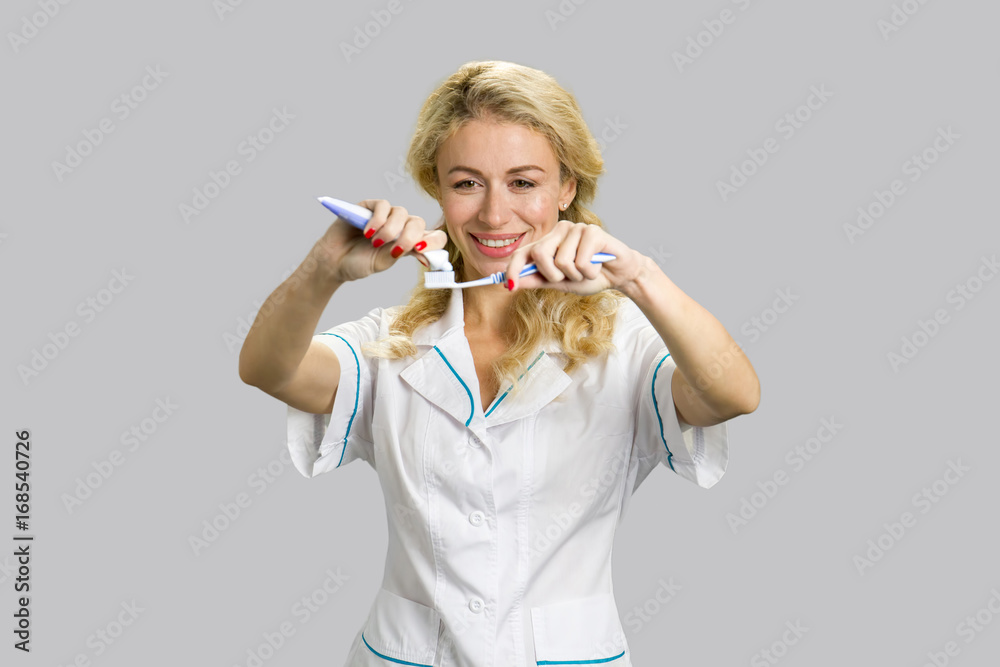 Cheerful girl applying toothpaste on toothbrush. Young beautiful female, smiling and preparing for brushing her teeth on grey background. Cheerful girl applying toothpaste on toothbrush. Young beautiful female, smiling and preparing for brushing her teeth on grey background.