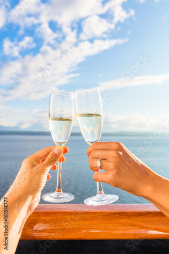 Luxury honeymoon cruise couple toasting champagne. Travel holiday newlyweds drinking with wedding rings holding glasses doing cheers at sunset view of cruise holiday destination.