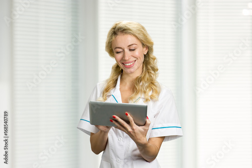 Smiling young nurse with computer tablet. Cheerful young medical doctor looking on computer tablet and smiling.
