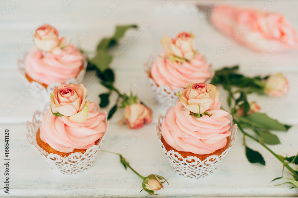 Delicate tasty muffins with a pink cream decorated with real roses on a wooden background