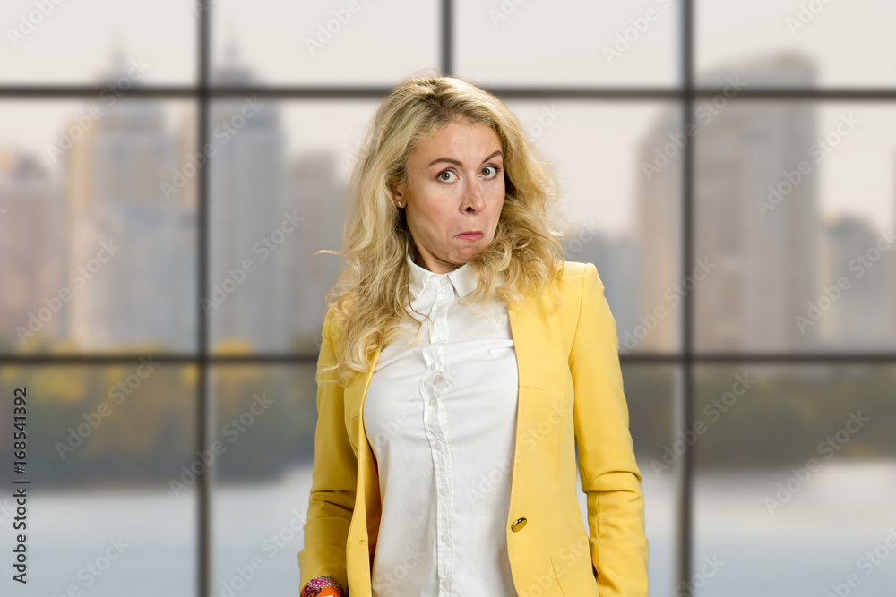 Fototapeta premium Surprised woman with funny grimace. Young business woman with stupor surprised funny face expression on office window background.