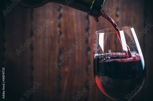 Pouring red wine into the glass against wooden background photo
