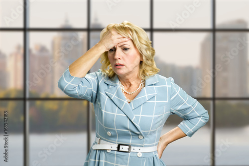 Worried woman on office background. Stressed busineswoman with headache, migraine or forgetfulness on office window background.