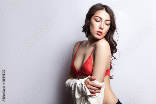 Young sexy body. Beautiful erotic young model on red bra, with vawy hair, undressing and closed eyes. Isolated on gray background, studio shot photo