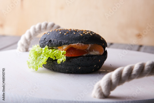 Black wooden serving tray with black burger, potato wedges and ketchup, vertical shot on a grey stone background photo