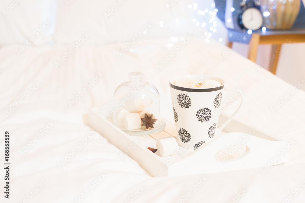 Breakfast in bed - wooden tray with cup of coffee and marshmallows, cozy hygge home style
