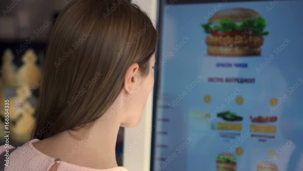 Beautiful attractive woman in pale pink in food court mall. Ordering food via self-service machine at fast-food chain restaurant