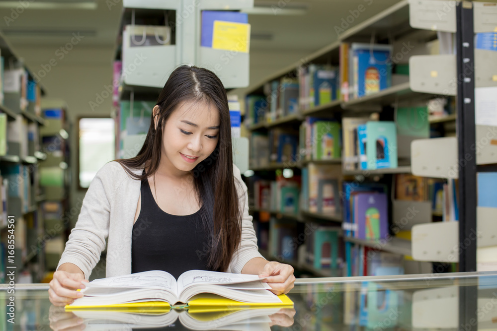 Woman in the foreground is Holding a books for reading. Young Asian Woman are reading Book in the modern library. People with Education concept. Woman in the foreground is Holding a books for reading. Young Asian Woman are reading Book in the modern library. People with Education concept.