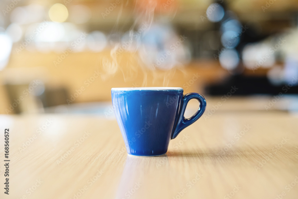 Fototapeta premium A blue cup of espresso coffee on wooden table in the background of cafeteria