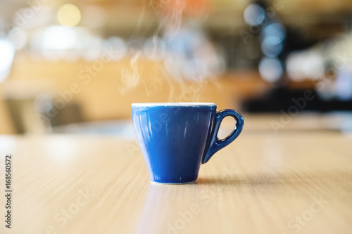 A blue cup of espresso coffee on wooden table in the background of cafeteria