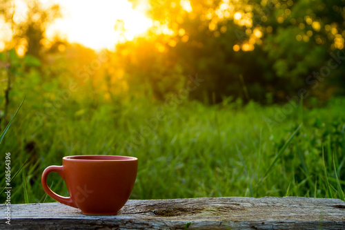 Morning cup of coffee on wooden table at sunrise