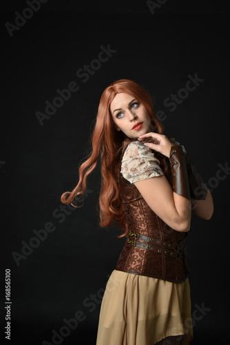 portrait of a red haired girl wearing steampunk costume. black studio background.