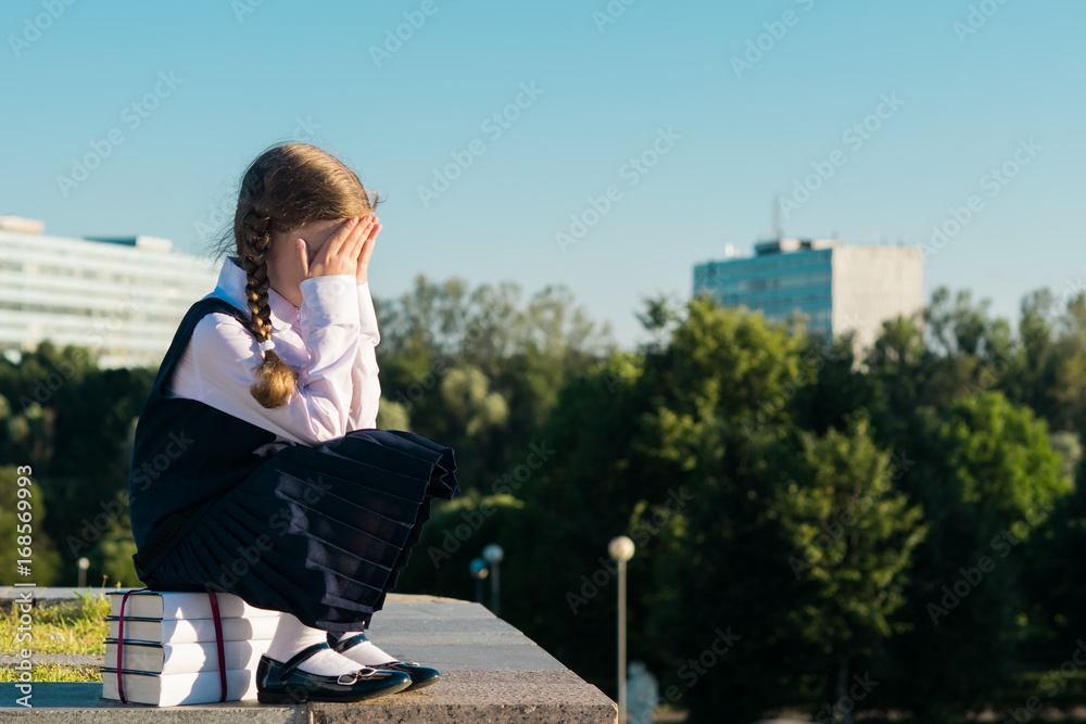 little schoolgirl sits on a textbook and cries, does not want to study